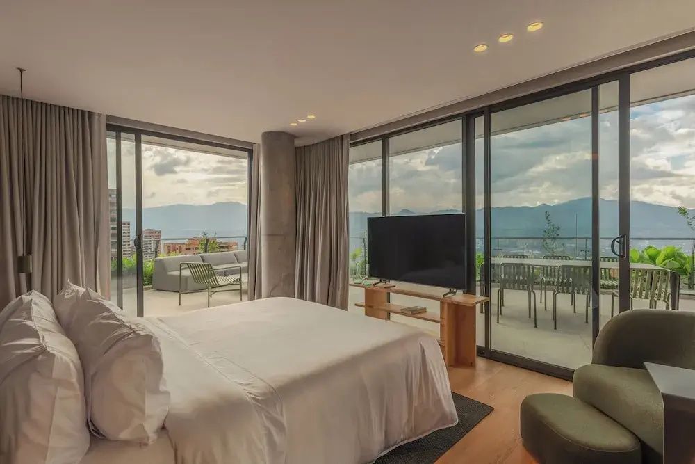 Schlafbereich mit großer Glasfront, Fernseher und Blick auf die Terrasse.