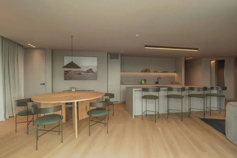 Runder Esstisch aus Holz mit Stühlen im hell gestalteten Wohnbereich des Apartments.