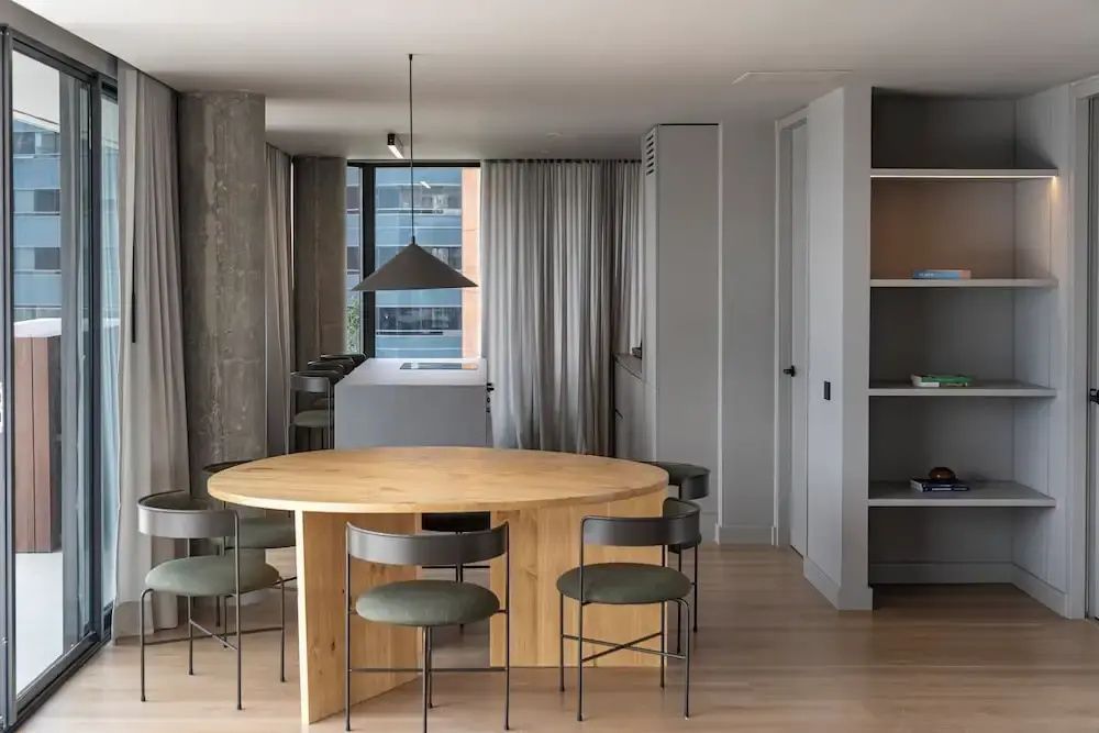 Runder Holztisch mit Stühlen in einem hellen, modern eingerichteten Zimmer mit Kücheninsel im Hintergrund.