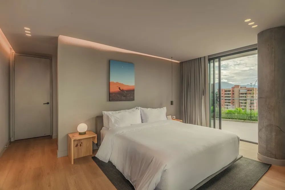 Modernes Schlafzimmer mit weißem Doppelbett, Wandbild und großem Fenster.