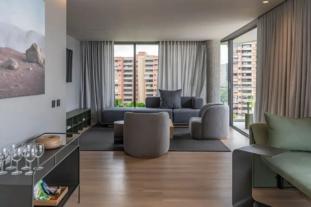 Möbliertes Wohnzimmer einer Suite mit grauem Sofa, Sesseln und großen Fensterfronten.