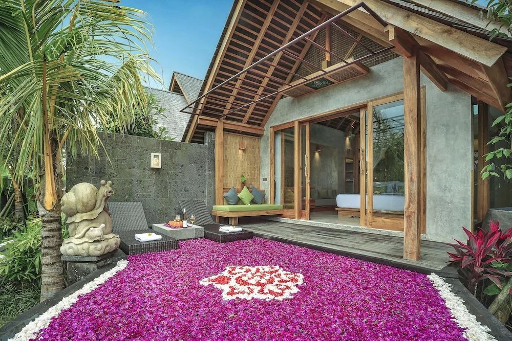 Überdachte Holzterrasse mit einem von rosa Blüten bedeckten Pool und Sonnenliegen.