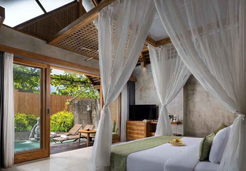 Helles Schlafzimmer mit großem Himmelbett, Fernseher und Blick auf den Außenbereich.