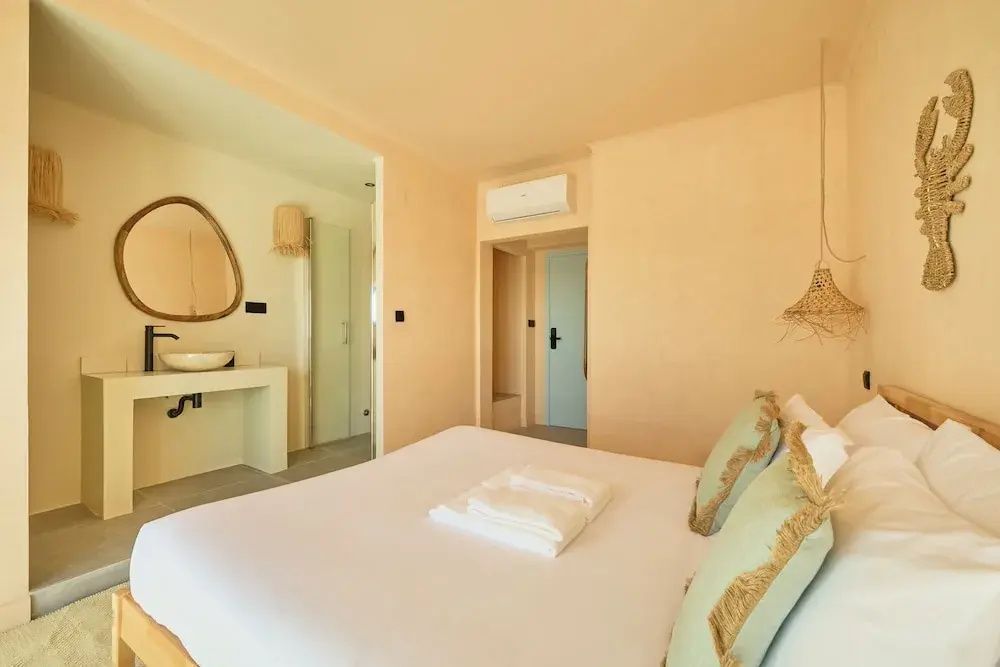 Helles Hotelzimmer mit weiß bezogenem Doppelbett, Klimaanlage und sanftem Wandanstrich.