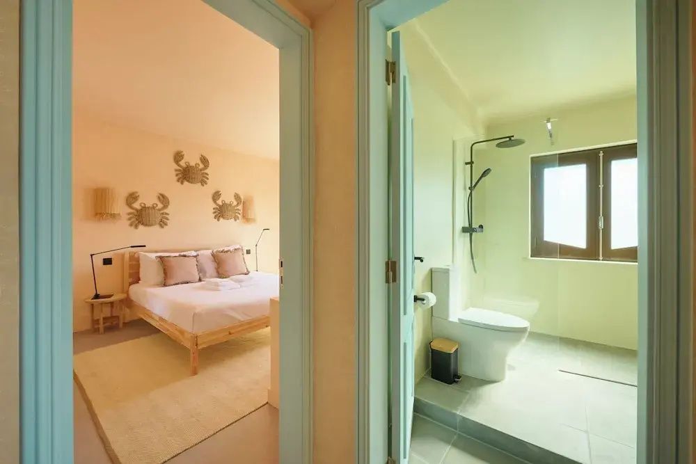 Blick durch zwei Türen in ein Schlafzimmer mit Doppelbett und das angrenzende Badezimmer.