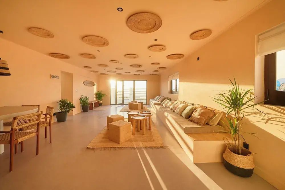 Lounge mit langer Sitzbank, Holzschemeln, Flechtteppichen und runder Deckendeko.