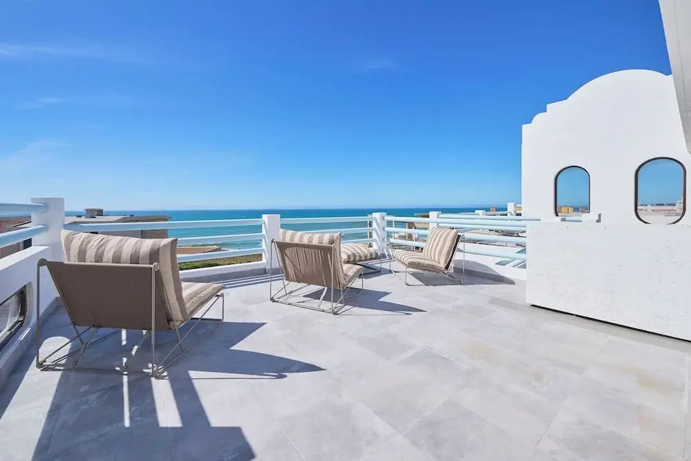 Dachterrasse mit Polstersesseln, weißem Geländer und freiem Blick auf das blaue Meer.