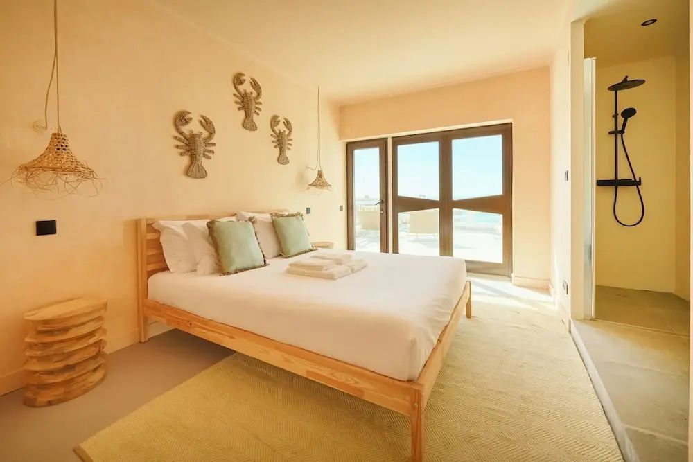 Schlafzimmer mit Holzbett, Wanddekoration und großem Fenster mit Blick nach draußen.