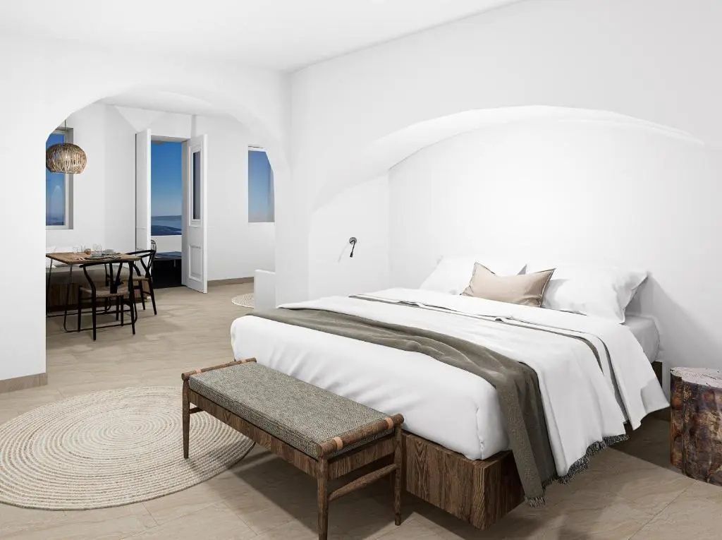 Helles Schlafzimmer mit Doppelbett, Holzbank und Blick durch die Tür auf das Meer.