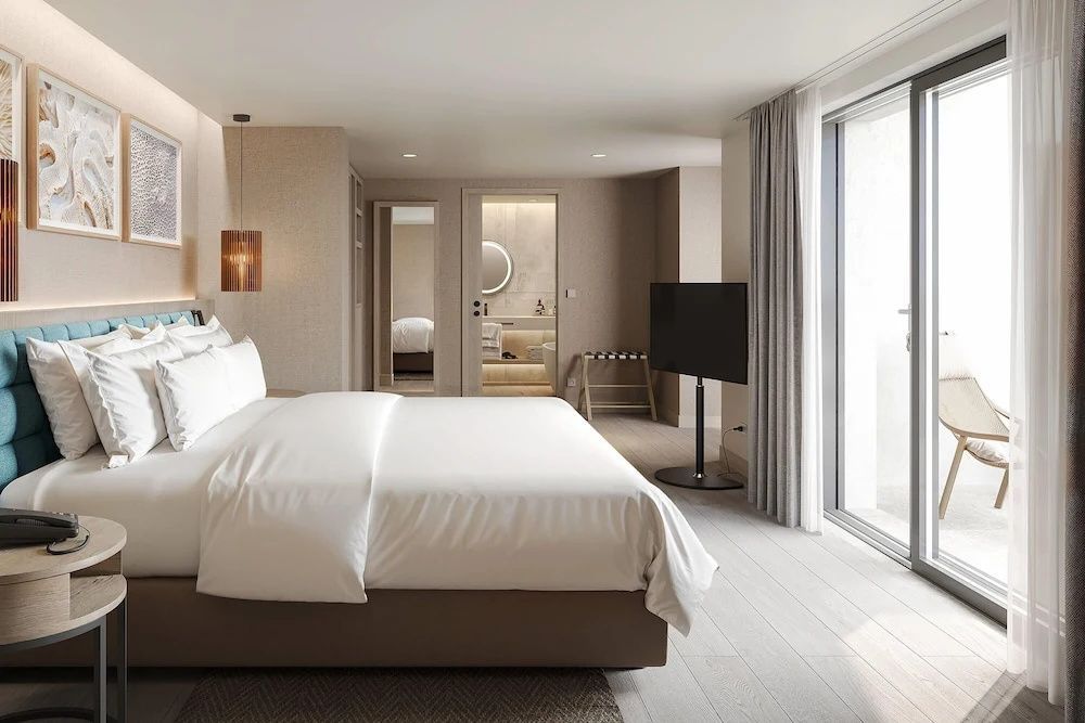 Helles Hotelzimmer mit großem Doppelbett, Fernseher auf Ständer und Durchgang zum Bad.