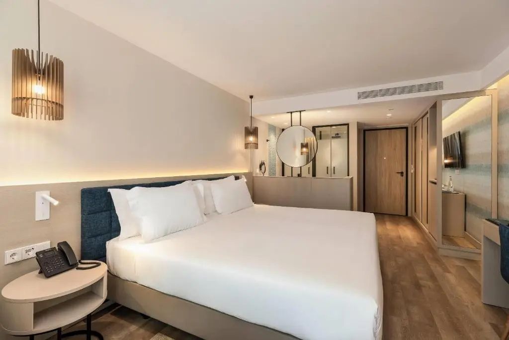 Doppelbett mit weißer Bettwäsche und gepolstertem Kopfteil in einem hellen Hotelzimmer.