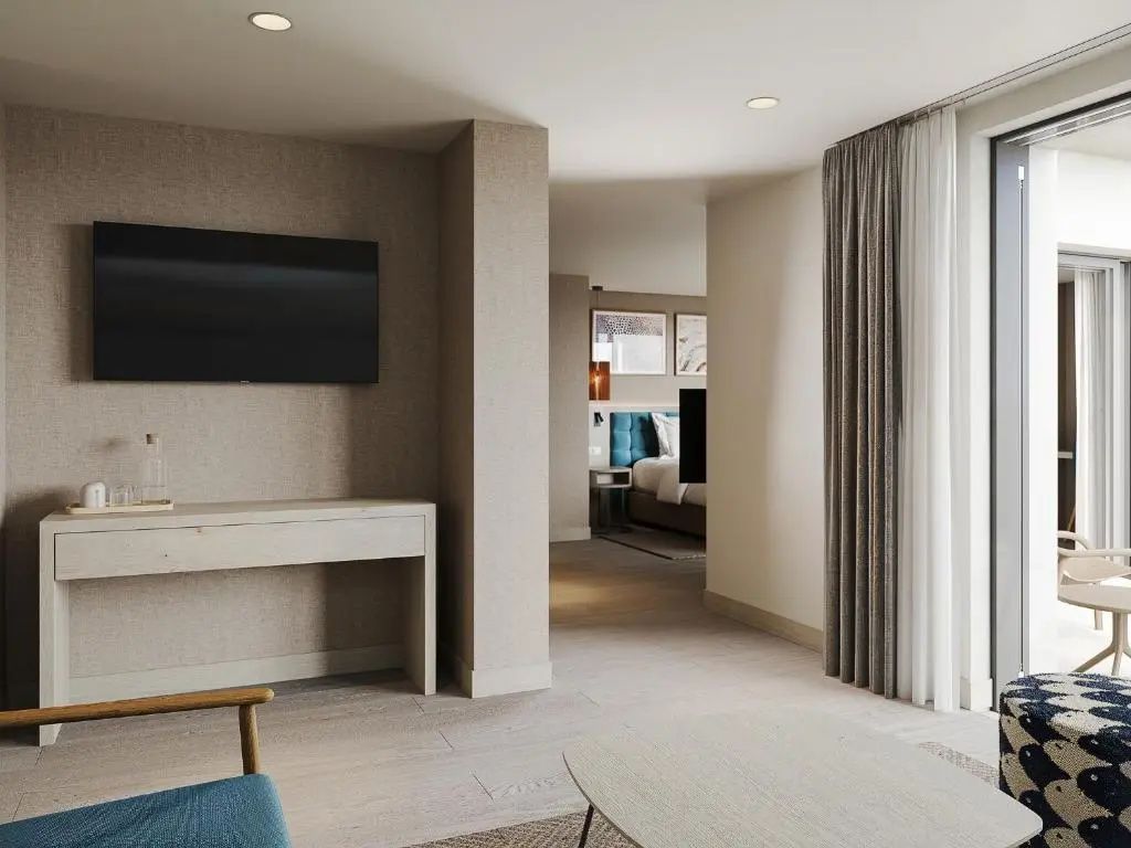 Heller Wohnbereich einer Hotelsuite mit Wandfernseher, Schreibtisch und Blick auf das Schlafzimmer.