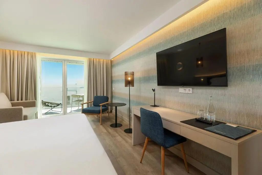 Modernes Hotelzimmer mit Schreibtisch, Fernseher und Balkonzugang mit Meerblick