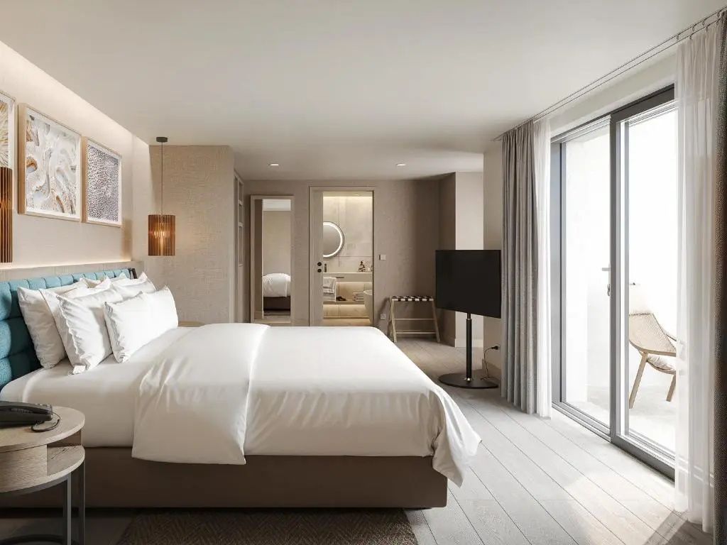 Hell eingerichtetes Hotelzimmer mit großem Doppelbett, Parkettboden und Zugang zum Balkon.