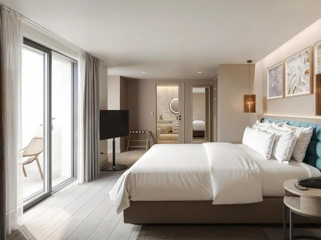 Geräumiges Schlafzimmer im Hotel mit weißem Doppelbett, Balkontür und Blick ins Badezimmer.