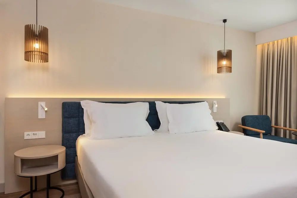 Doppelbett mit weißer Bettwäsche, blauem Kopfteil und einer Hängelampe im Hotelzimmer.
