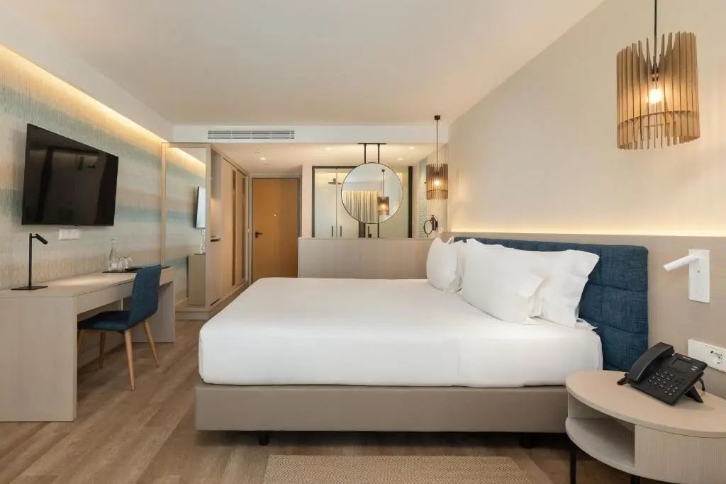 Hell eingerichtetes Hotelzimmer mit großem Doppelbett, Schreibtisch und Holzfußboden.
