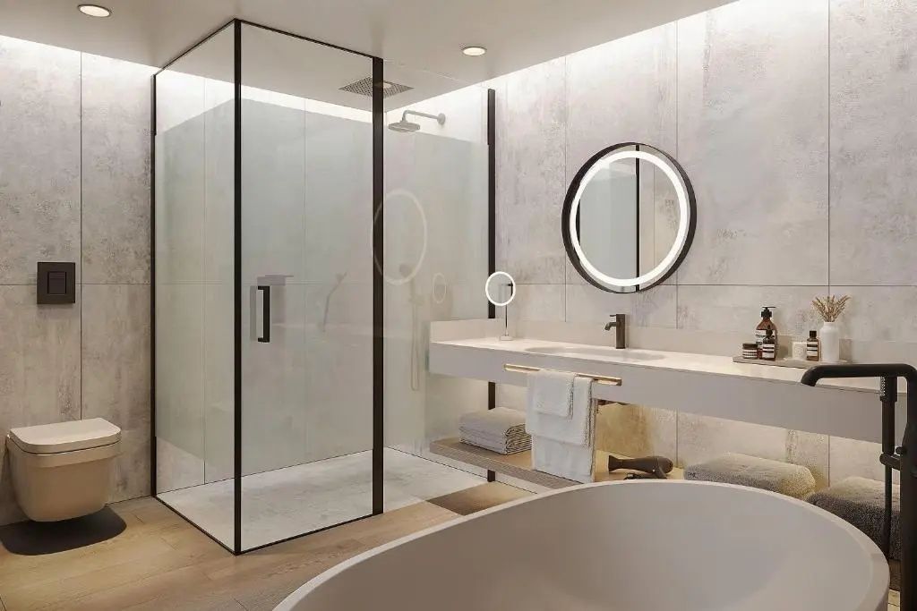 Badezimmer mit begehbarer Glasdusche, Waschtisch mit beleuchtetem Rundspiegel und Rand der Badewanne.