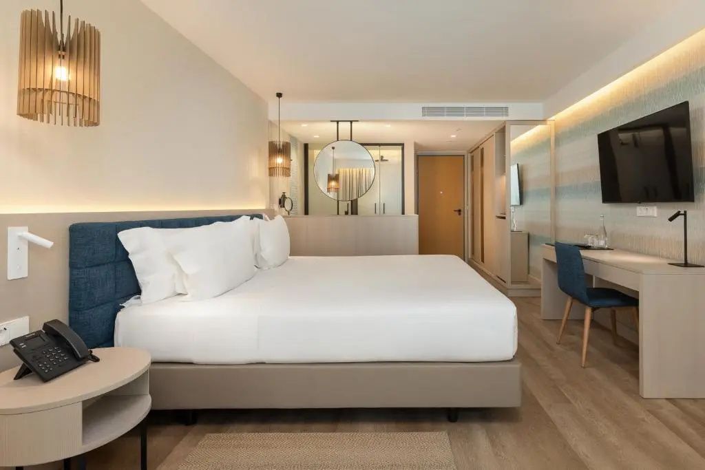 Blick in ein geräumiges Hotelzimmer mit Doppelbett, Parkettboden und Schreibbereich.
