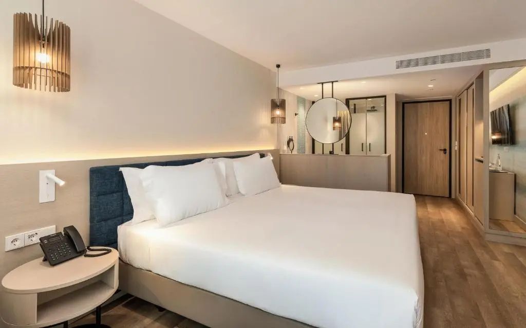 Doppelbett mit weißen Kissen im Hotelzimmer und Blick Richtung Badezimmer.