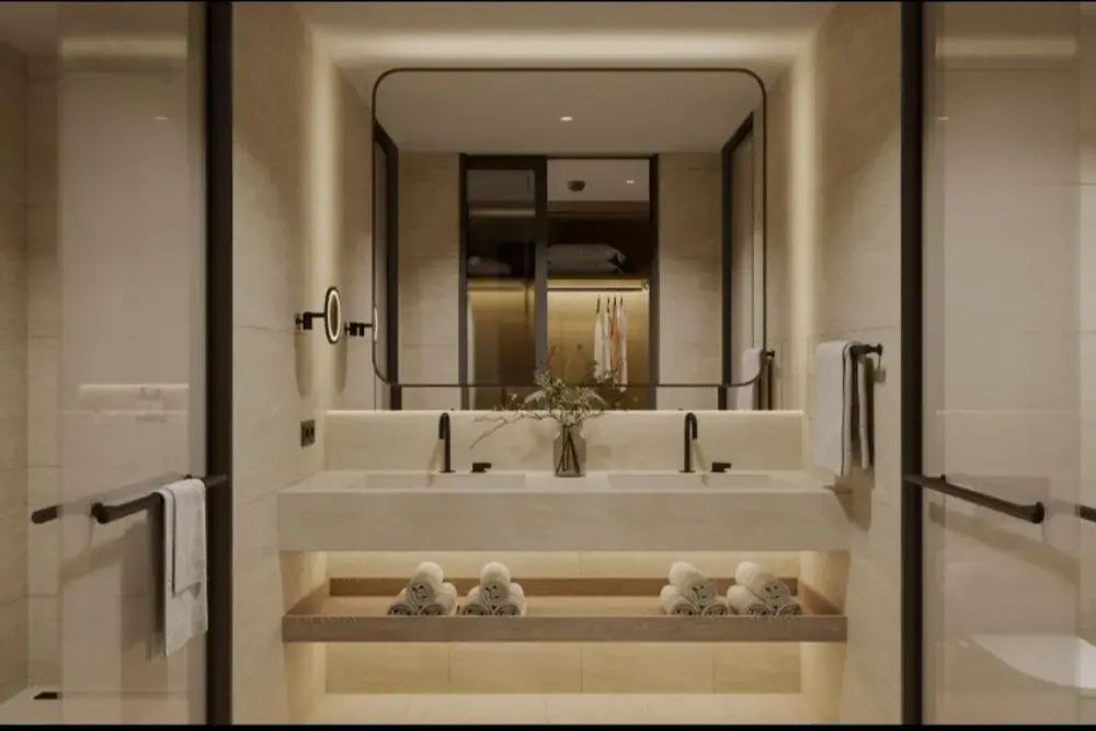 Badezimmer mit Doppelwaschbecken, großem beleuchteten Spiegel und eingerollten Handtüchern.