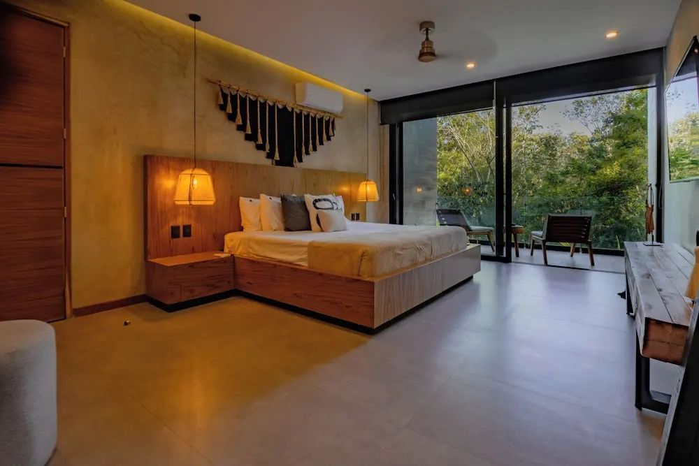 Doppelbett aus Holz mit Beleuchtung, Dekoration an der Wand und Zugang zum Balkon mit Blick ins Grüne.