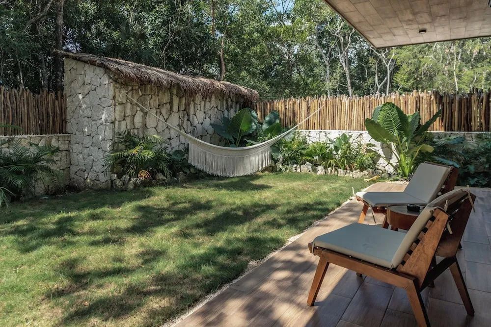 Private Terrasse mit Holzdeck, zwei Stühlen, Rasen und Hängematte vor einer Steinmauer.