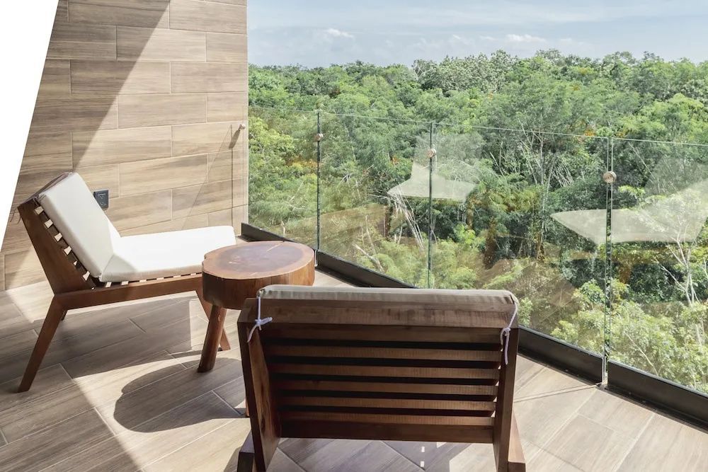 Balkon mit Holzstühlen und Glasgeländer sowie Blick auf dichte grüne Vegetation.