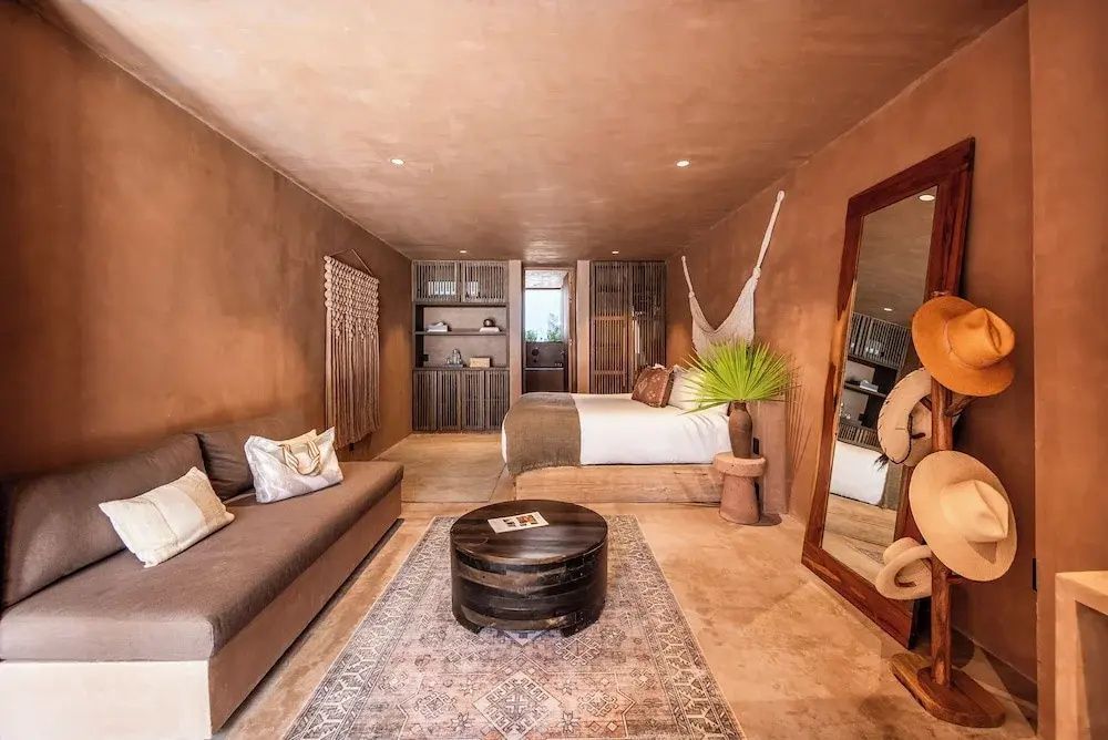 Geräumiges Zimmer im Erdton-Design mit Sitzbereich, Couch, Teppich und Doppelbett im Hintergrund.