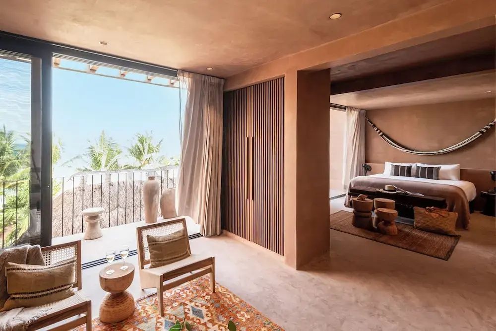 Geräumiges Hotelzimmer mit Sitzbereich, Holzschrank und Balkon mit Palmenblick.
