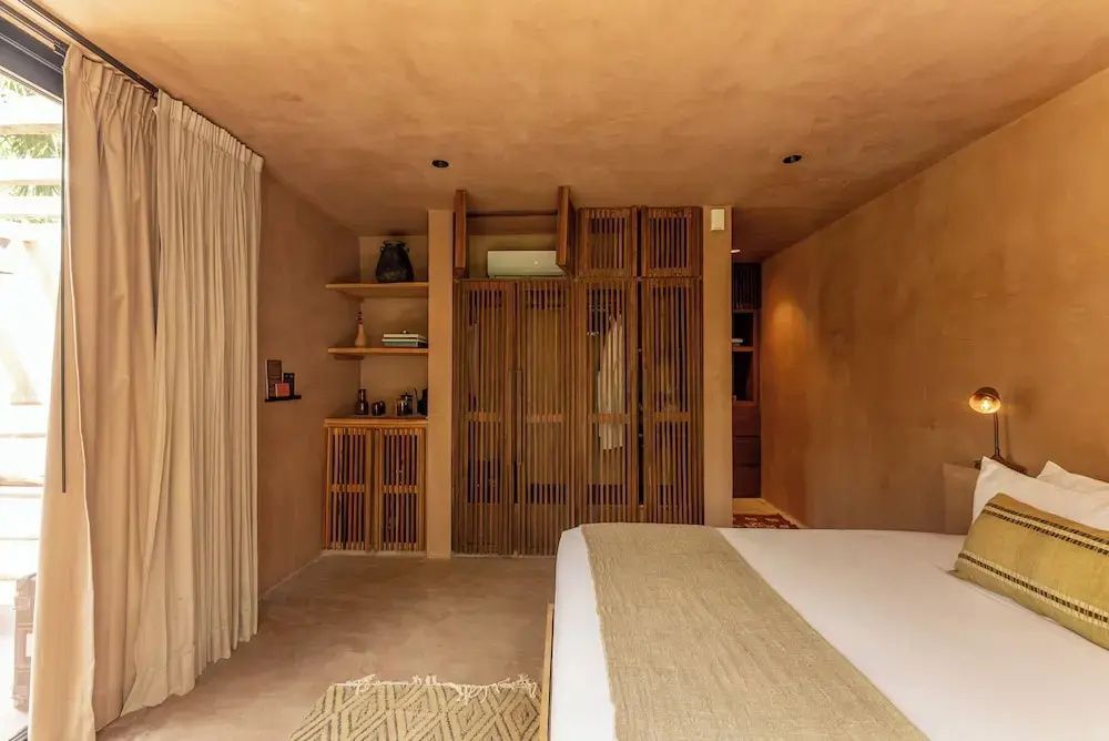 Blick auf den Einbauschrank aus Holz und die Regale in einem hellbraun gestalteten Hotelzimmer.