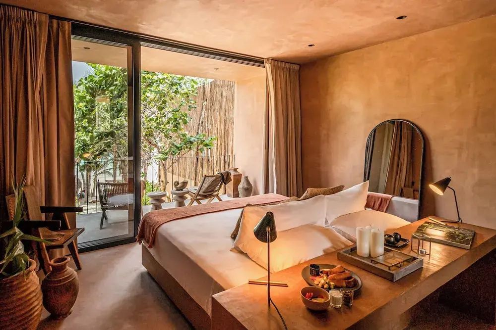 Doppelbett im Hotelzimmer mit Blick auf die Terrasse und tropische Pflanzen.