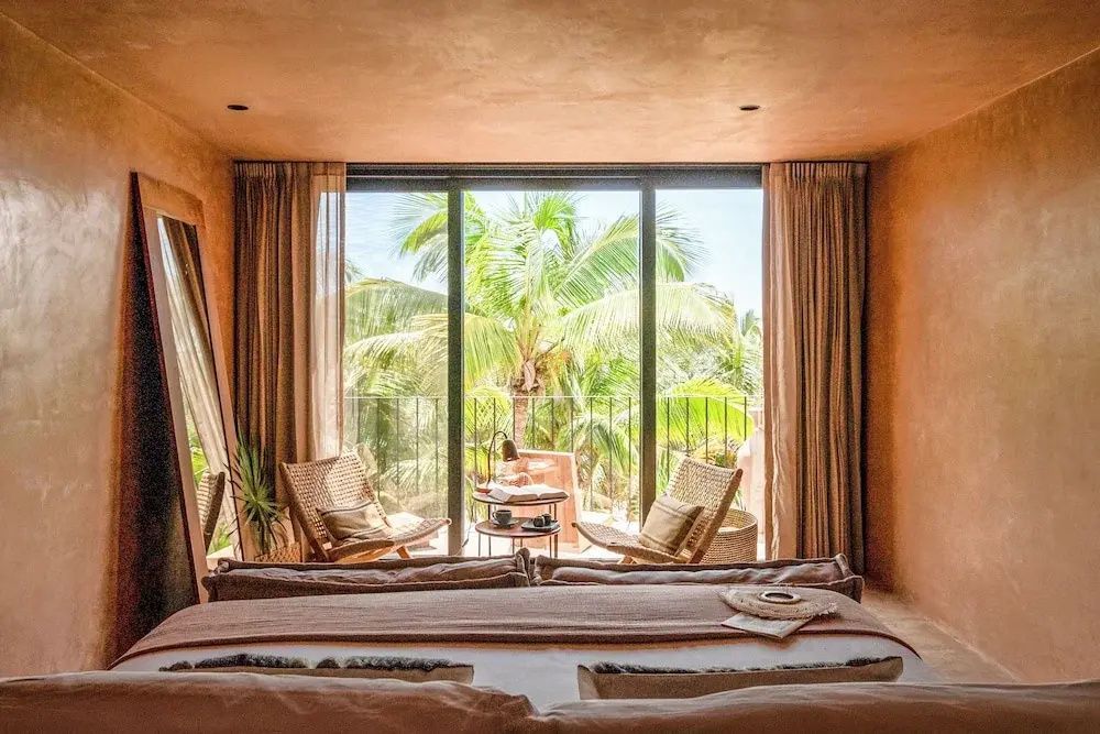 Hotelzimmer mit Balkon und Blick auf Palmen sowie tropische Pflanzen.