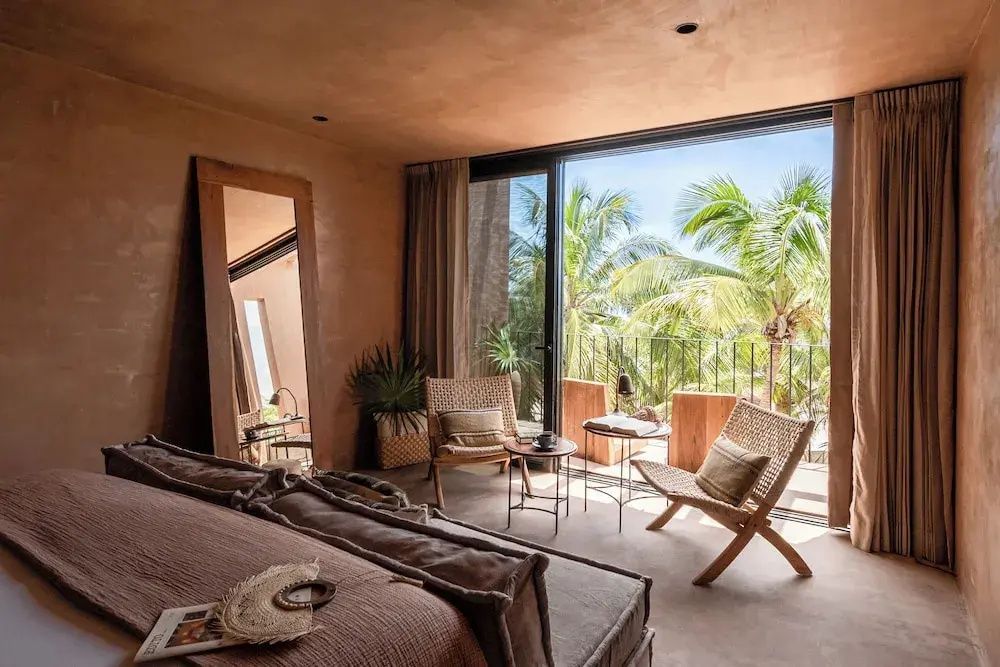 Schlafzimmer mit großem Bett, Standspiegel und Zugang zur Terrasse mit Palmenblick.