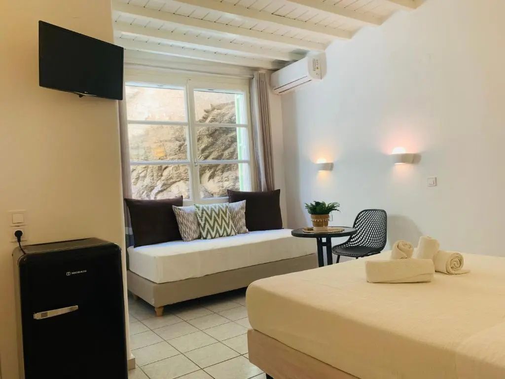 Modernes Hotelzimmer mit hellem Bett, einer Couch am Fenster und Wandleuchten.