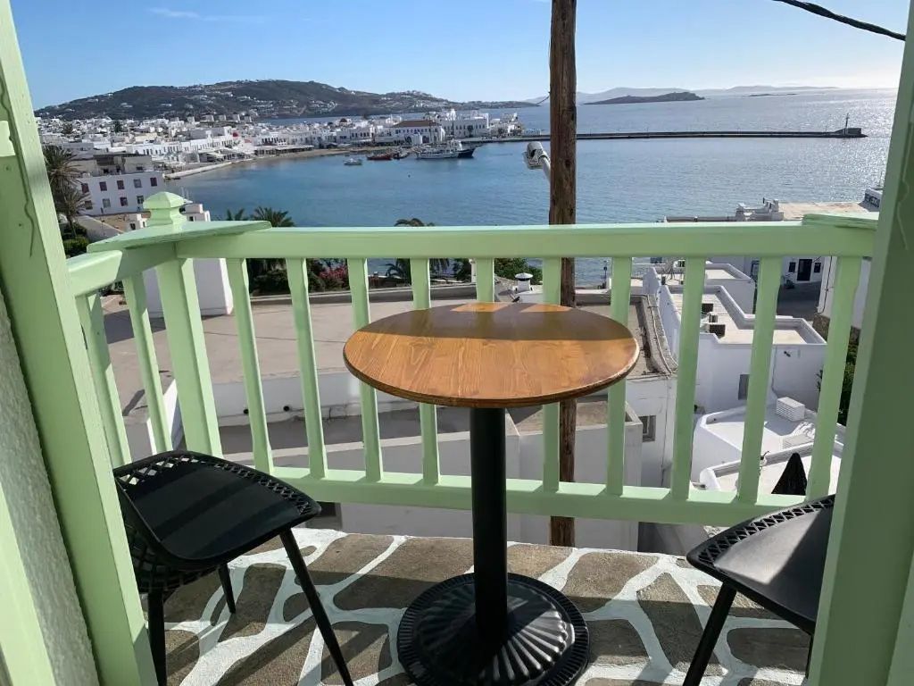 Balkon mit Holztisch und Stühlen sowie Blick auf die Stadt am Meer.