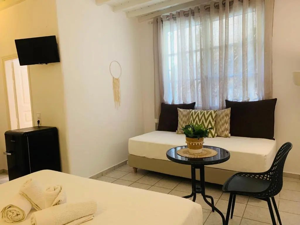 Hotelzimmer mit weißem Sofa, Beistelltisch, Pflanze und verhängtem Fenster.