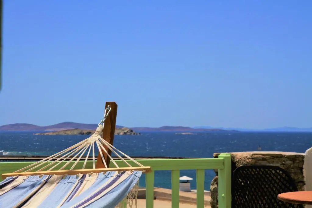 Eine Hängematte auf der Terrasse mit Blick über ein grünes Geländer auf das Meer.
