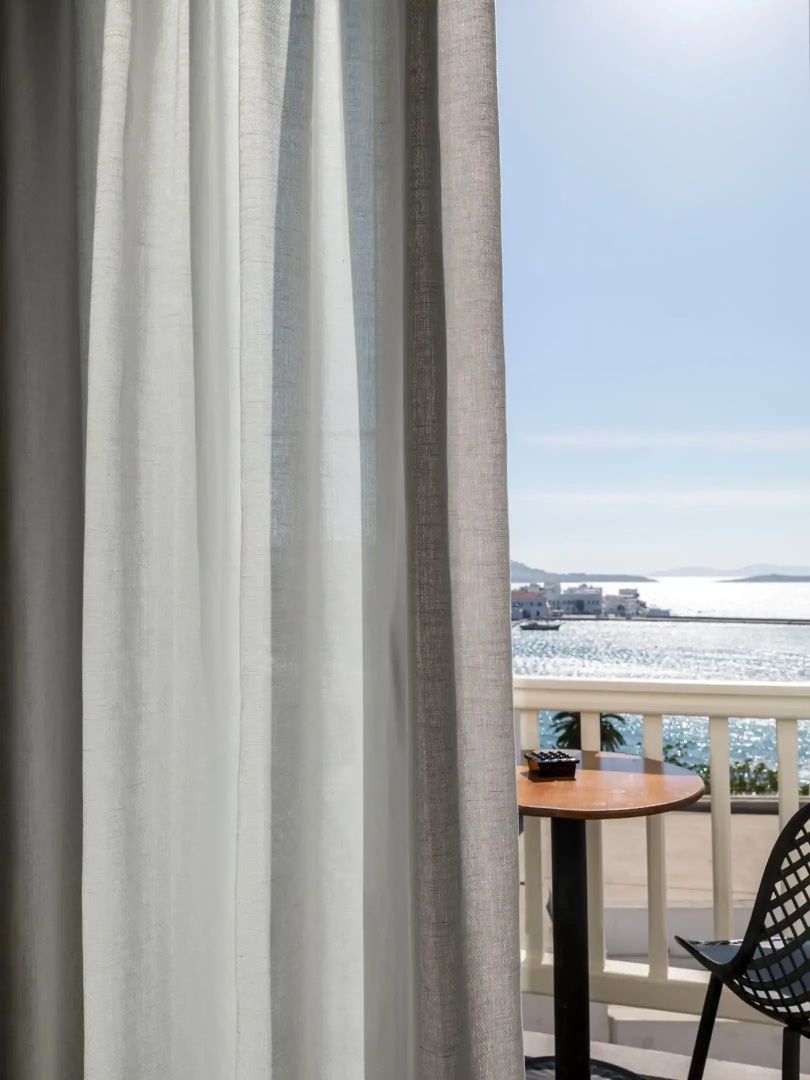 Ausblick vom Balkon durch helle Vorhänge auf das Meer und die gegenüberliegende Küste.