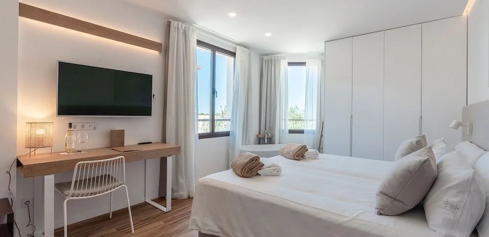 Helles Hotelzimmer mit Doppelbett, Schreibtisch, Fernseher und frei stehender Badewanne am Fenster.