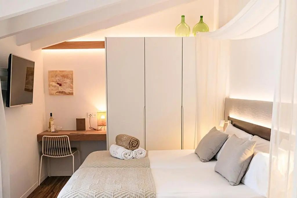 Helles Hotelzimmer mit Doppelbett, weißem Kleiderschrank und kleinem Schreibtisch am Fenster.