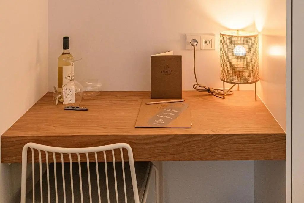 Holzschreibtisch im Hotelzimmer mit Tischlampe, Informationsmappe und einer Flasche Wein.