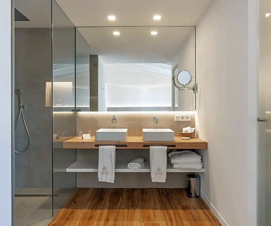 Modernes Badezimmer mit zwei Waschbecken auf Holztisch, großem Spiegel und Glasdusche.