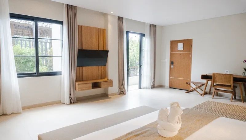 Hell eingerichtetes Hotelzimmer mit Wandfernseher, Holztür und Balkonausgang.