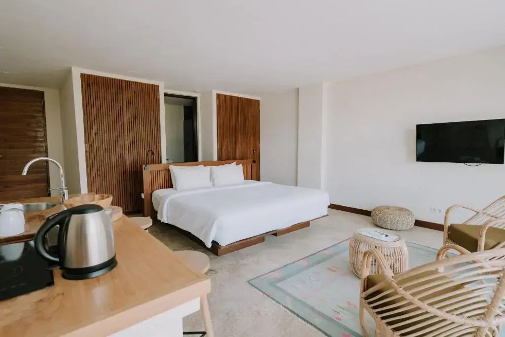 Helles Hotelzimmer mit einem großen Doppelbett, Holzkopfteil und Rattanmöbeln.
