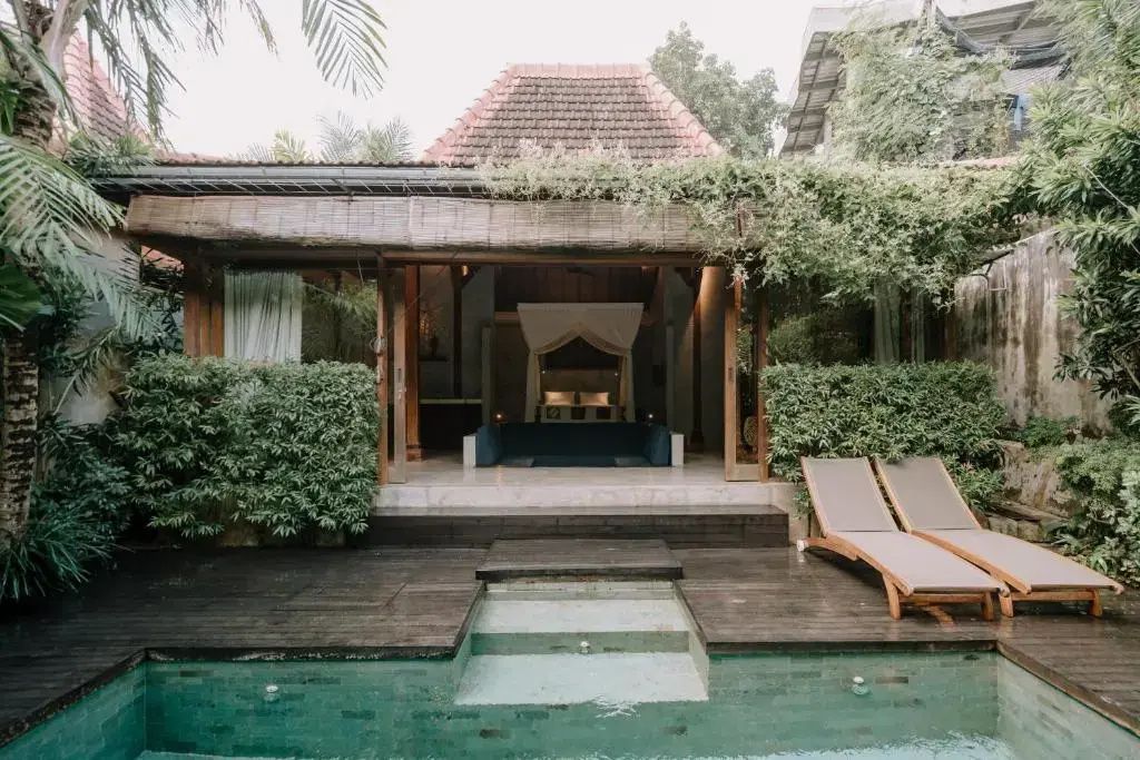 Privater Pool vor einer offenen Villa mit Holzterrasse und zwei Sonnenliegen.