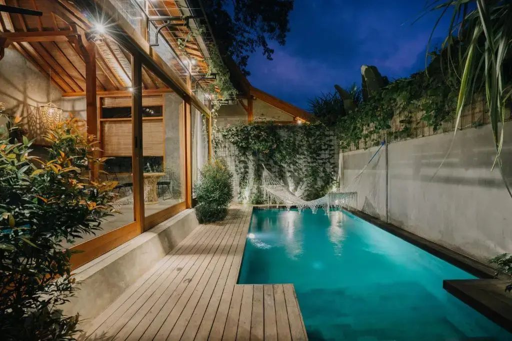 Beleuchteter Außenpool bei Nacht mit Holzdeck und Hängematte neben der Villa.