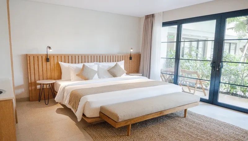 Doppelbett mit Holzkopfteil und Sitzbank vor einer großen Glasschiebetür.