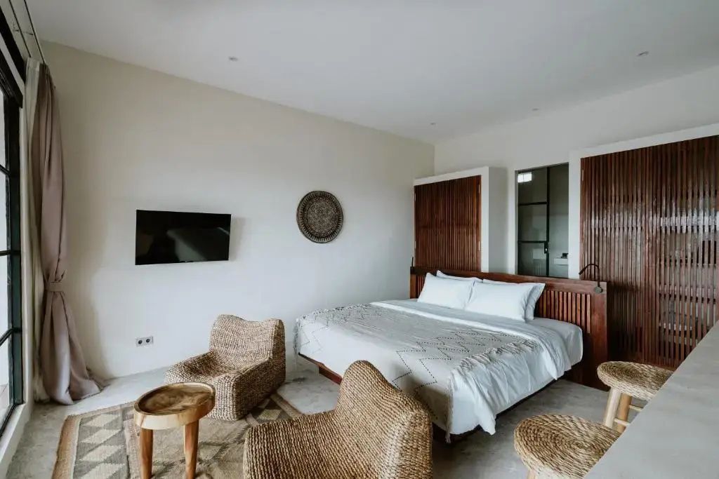 Zimmer mit einem großen Doppelbett, Fernseher an der Wand und Flechtstühlen.