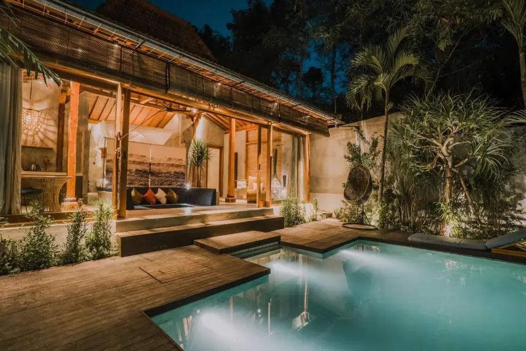 Beleuchtete Villa bei Nacht mit Holzterrasse, Sitzbereich und Außenpool.